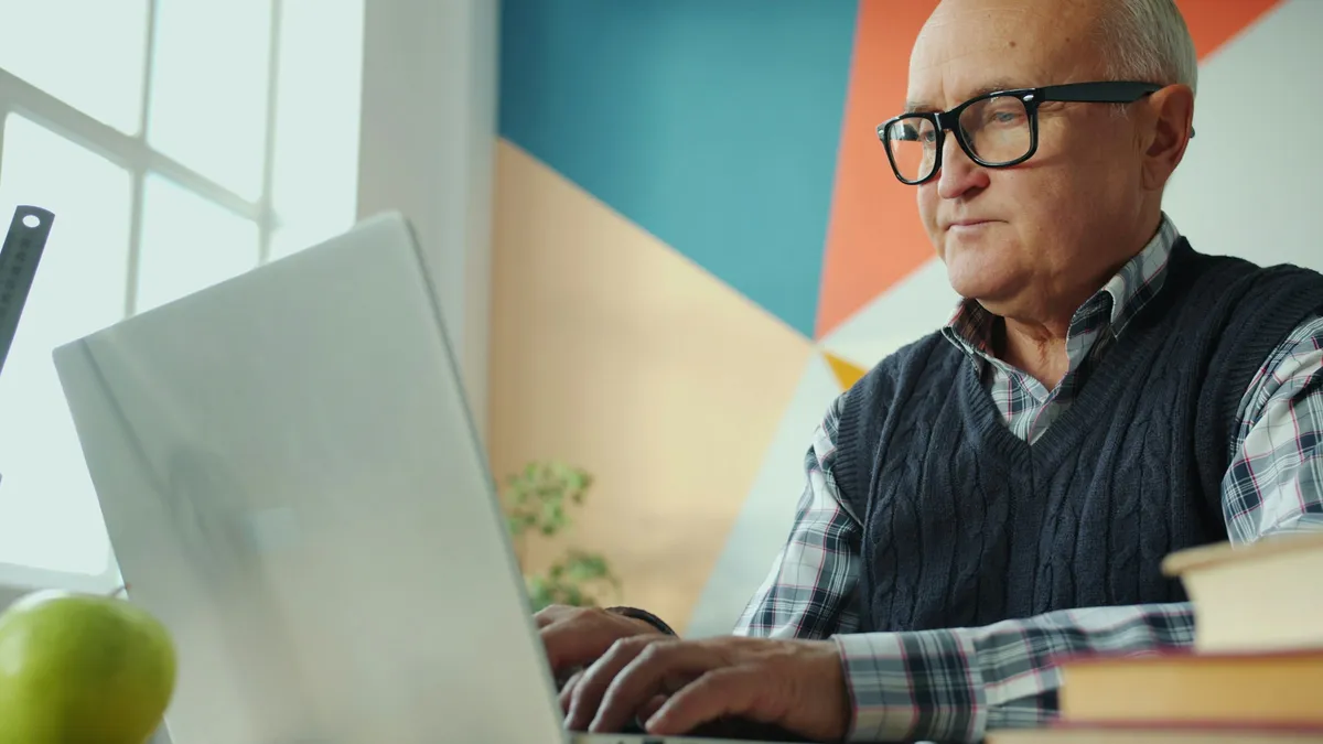 An older man in glasses typing on a laptop at a table